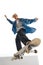 Dynamic image of teen boy in blue shirt and capo training, in motion, skateboarding  over white background
