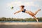 Dynamic image of young woman in motion, playing beach volleyball, hitting ball and falling down on sand