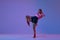 Dynamic photo of athletic teen girl, mma fighter in sportswear training against purple studio background in neon lights