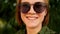 Dynamic video. A close-up portrait of a red-haired girl in sunglasses against the backdrop of summer greens. Natural