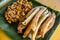 Dynamite lumpia and Tofu in peanut garlic sauce placed on a tray lined with banana leaves.