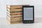 E-reader near stack of paper books on a white wooden table. Copy space on e-book display. E-reading on anti-glare screen for