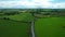 Eagle eye view of a car driving down a narrow Irish countryside road with green fields in every direction