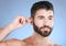Ear, cleaning and man with cotton bud in studio for hygiene, grooming and beauty routine on blue background. Earwax