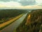 Early autumn morning on rocks above big river, fresh blue cloud in the sky, lights in town on river banks. Green forests in