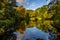 Early autumn view of a pond surrounded by autumnal coloured trees.buret through the trees..