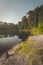 Early morning view of lake with trees around it. sand in foreground and reflections in the water