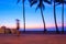 An early morning walker is blurred as he passes between two silhouetted palm trees created by the colorful sunrise