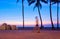 An early morning walker is blurred as he passes between two silhouetted palm trees created by the colorful sunrise