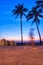 An early morning walker is blurred as he passes between two silhouetted palm trees created by the colorful sunrise