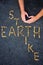 Earth strike - message written with tiny stones on a black sand background. Hands with a symbol of love