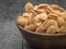 An earthenware bowl with unpeeled almonds on a black wooden table