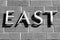 East sign, all caps on a brick wall