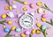 Easter alarm clock with colorful eggs and tulips on purple background.