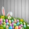 Easter background with bunny ears, flowers and colored decorated eggs in the grass on a wood background