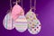 Easter background handmade. Group of colored eggs made of paper hang on a rope on a purple background.