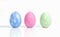 Easter blue, pink and green colored decorated eggs stand in a row on white background. with reflection. Minimal easter concept.
