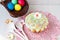 Easter cake on a table on a pink napkin, wooden spoons and a basket with colored eggs