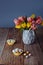 Easter candies covered eggs in various pastel colors in paper baskets near vase with fresh tulips on rustic wooden table and dark