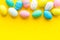 Easter composition. Decorated pastel Easter eggs on yellow background copy space border