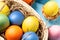 Easter composition - several colored eggs in a basket on a blue wooden table, top view