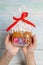 Easter decoration. Female hands holding gingerbread Easter cake packed in cellophane as gift on wooden backdrop