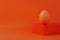 Easter egg on geometrical shape podium stage orange background Brown chicken egg balancing pedestal isometric minimalism