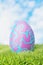 Easter egg in the grass in the meadow. Pink Easter egg in blue patterns. 3d render