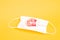 Easter egg in thermal sticker with a red pattern lies on a white medical protective child mask, yellow background