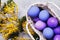 Easter eggs in a basket painted in different colors with a branch of mimosa on the table