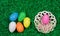 Easter eggs of different colors glittering in green grass and decorative bowl.