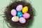 Easter eggs of different colors in a nest on a green background, top view