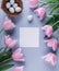 Easter eggs in nest, pink tulips flowers and sheet of paper over light blue background. Greeting card for Happy Easter. Flat lay,