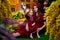 Easter. Family in rural wooden interior with flower in studio. Mother and daughter in maroon or red dresses of the