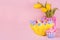 Easter festive background - yellow, blue, red eggs in yellow basket, tulips, cupcake on pastel pink background with copy space.