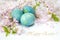 Easter greetings in English. Painted eggs with flowering twigs on a light background. Spring and holidays.