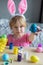 Easter holiday craft at home. Little girl in Easter bunny ears painting colored eggs