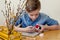 Easter Holiday at Home. Young blonde boy coloring drawing Easter Eggs