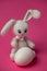 Easter knitted rabbit with a painted egg on a pink background. Concept of the Easter holiday.ok