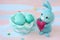 Easter light blue bunny sewn hands with a heart in its paws near the fabric basket with blue-white eggs. Greeting card for Happy