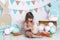 Easter! Little girl in overalls sits with a large Easter egg. Easter location, decorations. Family holidays, traditions. Colorful