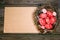 Easter red eggs with white pattern inside bird nest on right side of old sheet of paper on wood board. Top view horizontal