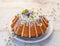 Easter yeast cake Babka covered with icing and decorated with edible flowers on a white plate on a white wooden table.