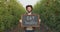 Eat healthy concept. Young positive man gardener showing board with slogan to camera, posing between apple trees