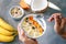 Eating healthy breakfast yogurt bowl with granola and fruits persimmon, banana, coconut and seeds. Male hands holding bowl with yo