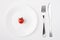 Eating on a low calorie concept. Top above overhead view photo of a plate with a single tomato with fork and knife placed to the