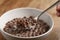 Eating with spoon chocolate cereal balls with milk in white bowl for breakfast on wooden table