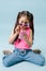 Eccentric dressed up tween girl in pink shirt and round sunglasses using phone