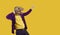 Eccentric showman in dinosaur mask and velvet jacket pointing index finger on yellow background.