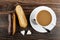 Eclairs with chocolate and peanut, pieces of sugar, coffee with milk in cup, spoon on saucer on wooden table. Top view